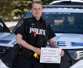 female officer in uniform standing in front of cruiser holding a sign