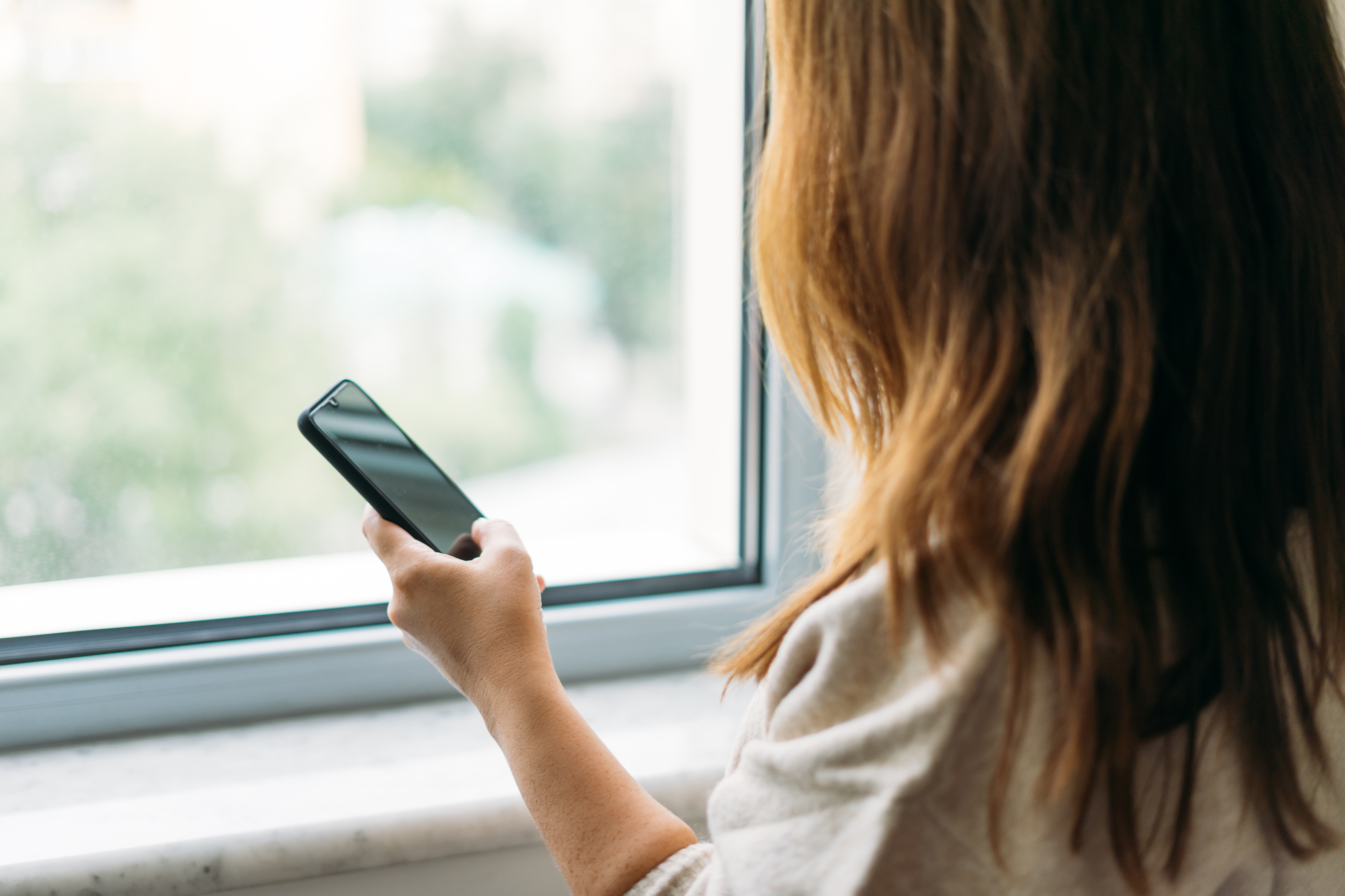 Woman Using Smartphone By Window Indoors